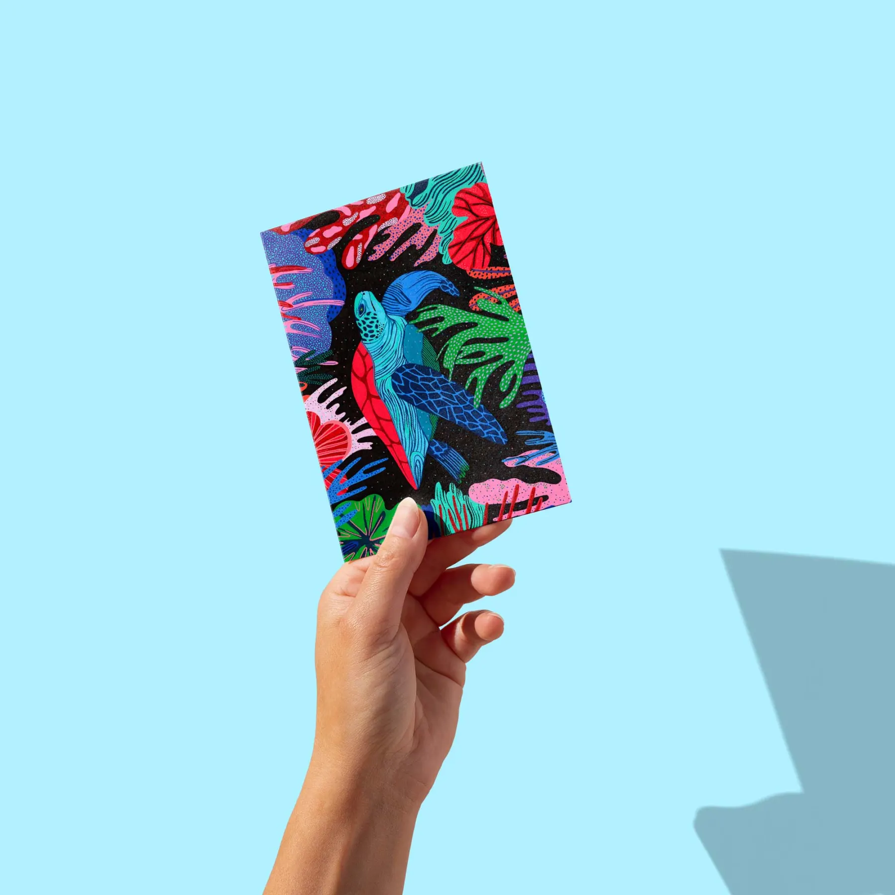 Tortue de mer bleue et rouge nageant parmi des coraux multicolores sur fond noir, carte postale illustrée par Orane Sigal