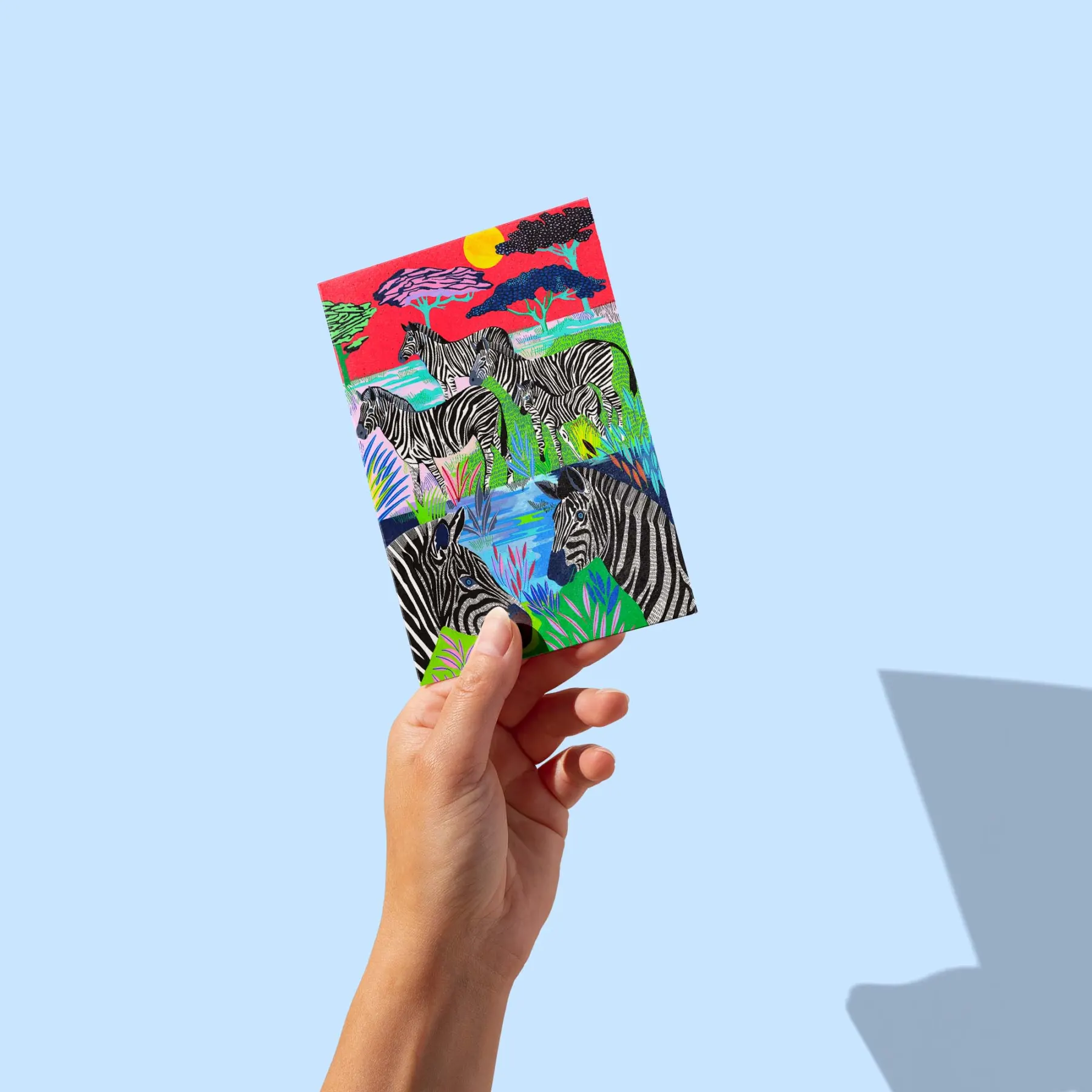 Troupeau de zèbres près d'un point d'eau dans une savane au ciel rouge et soleil doré, carte postale illustrée par Orane Sigal