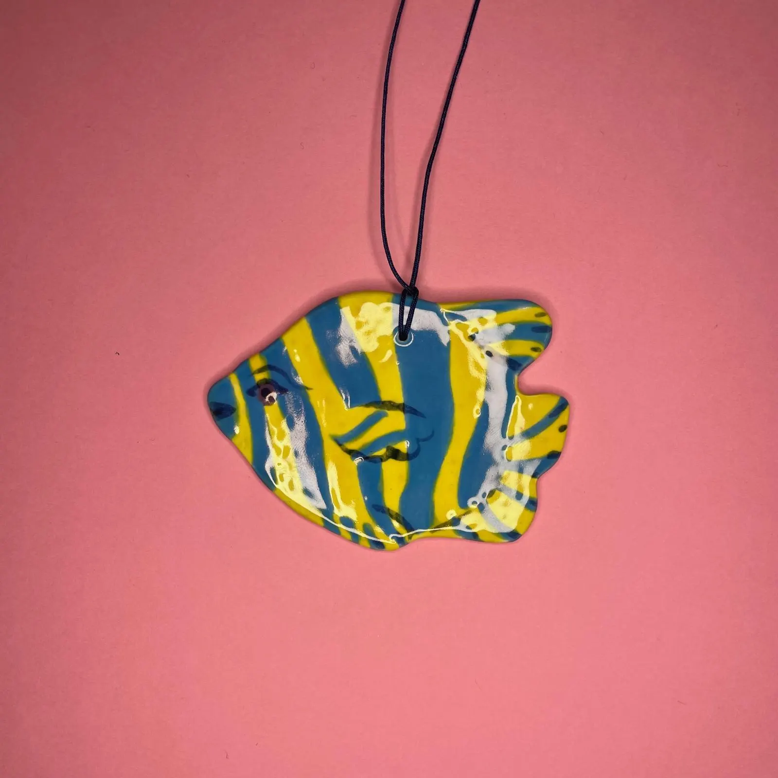 Suspension céramique en forme de poisson rayé jaune et bleu, fond rose, illustration par Orane Sigal