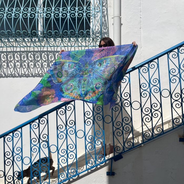 Grand papillon bleu et violet aux ailes ornées, fond floral coloré, illustration par Orane Sigal